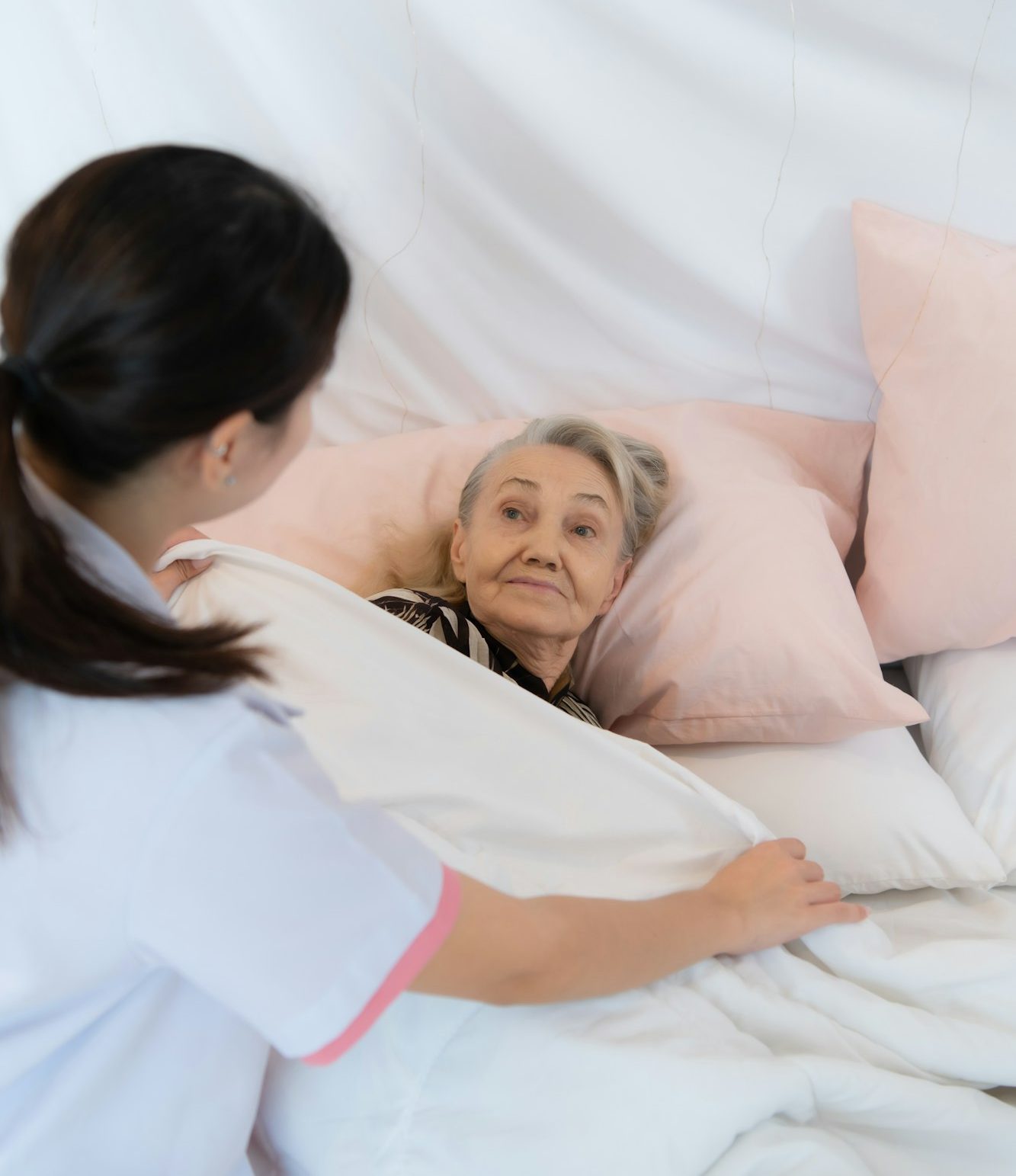 Caregiver for an elderly woman blanket the elderly woman on the bed